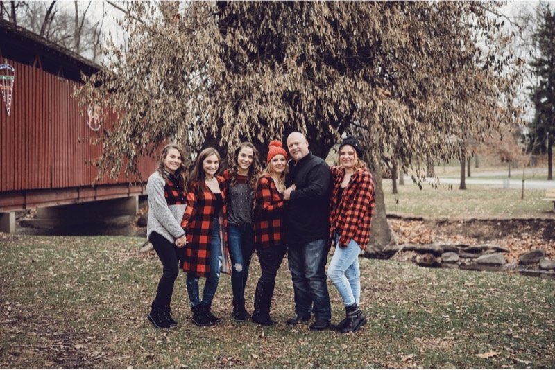 Scott Howell and family standing together under a willow tree near a covered bridge