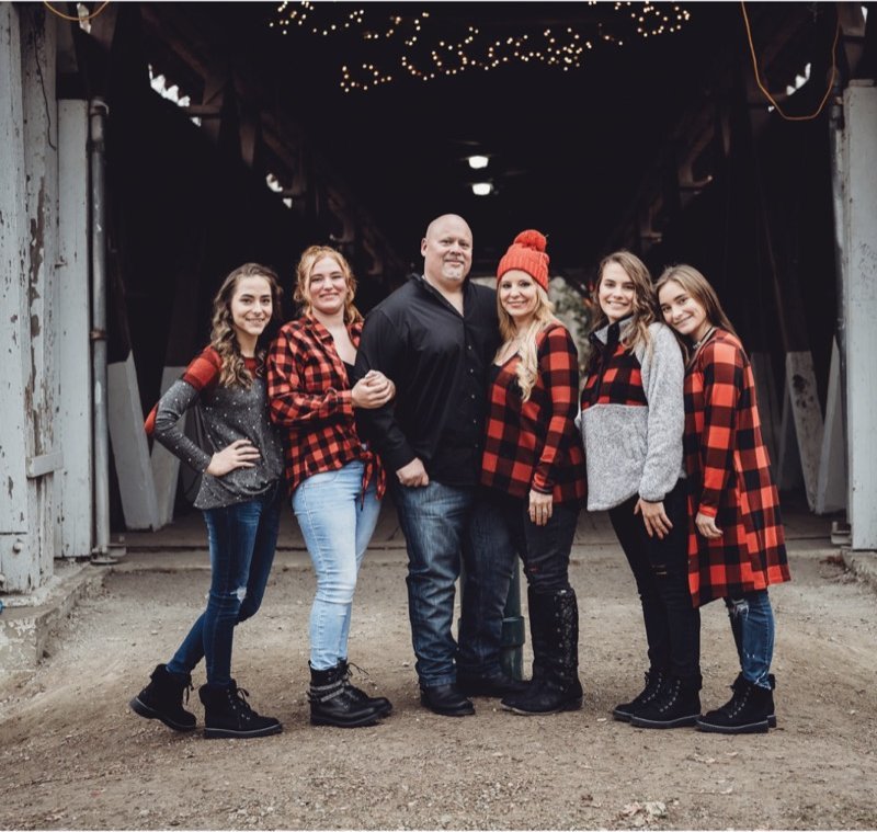 Scott Howell with his wife and four daughters in coordinated plaid outfits at a rustic barn